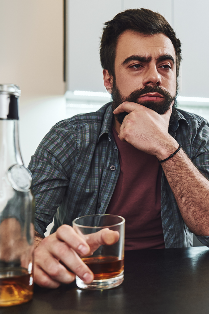 Thoughtful man holding a glass of whiskey, symbolizing the need for alcohol de-addiction support.